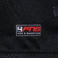 Detailed view of woven FNS logo label at the hem of the Fubar Jersey in Black.