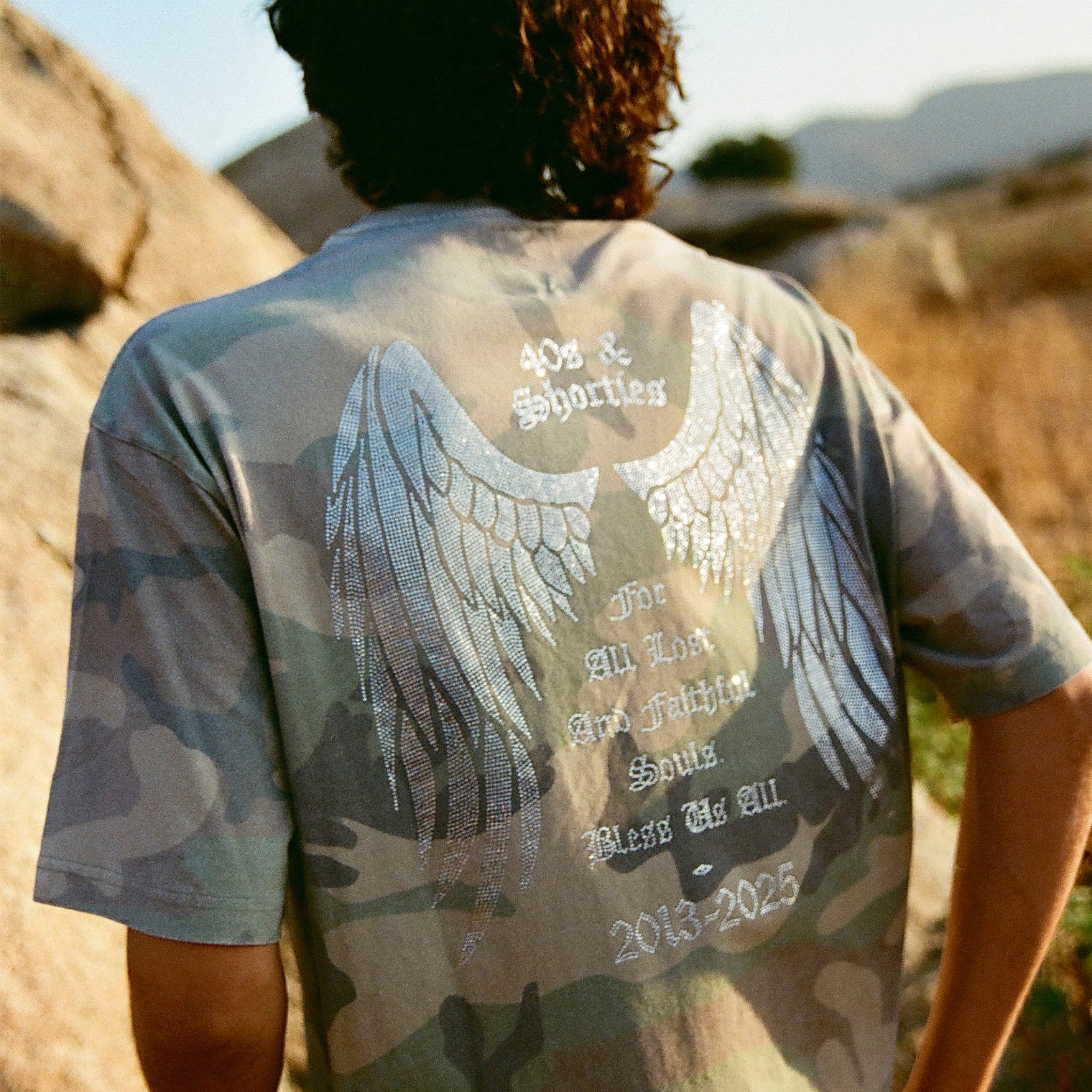 Back of 40s & Shorties Angel Wings Tee camo showing rhinestone angel wings graphic and tribute text.
