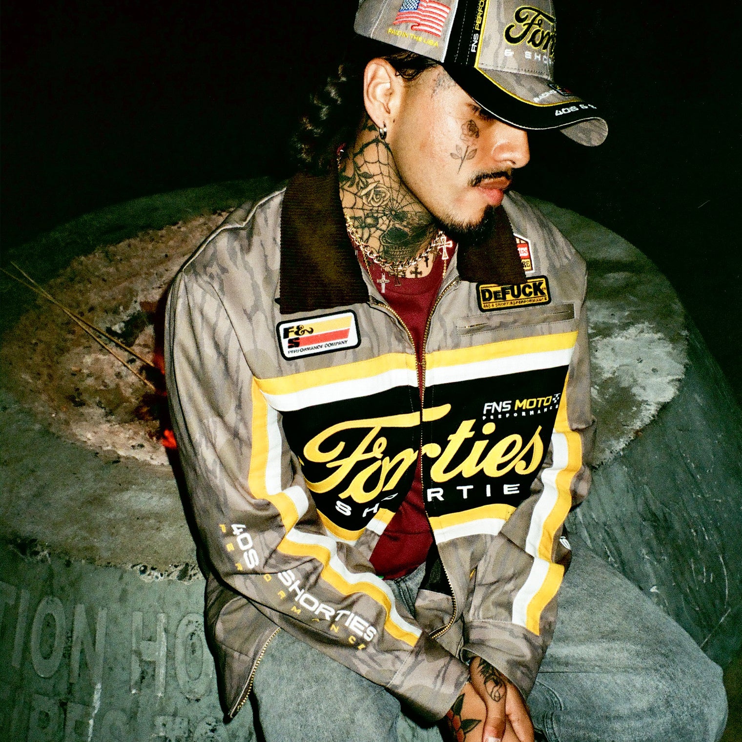 Man wearing 40s & Shorties Camo Garage Jacket and matching hat near fire