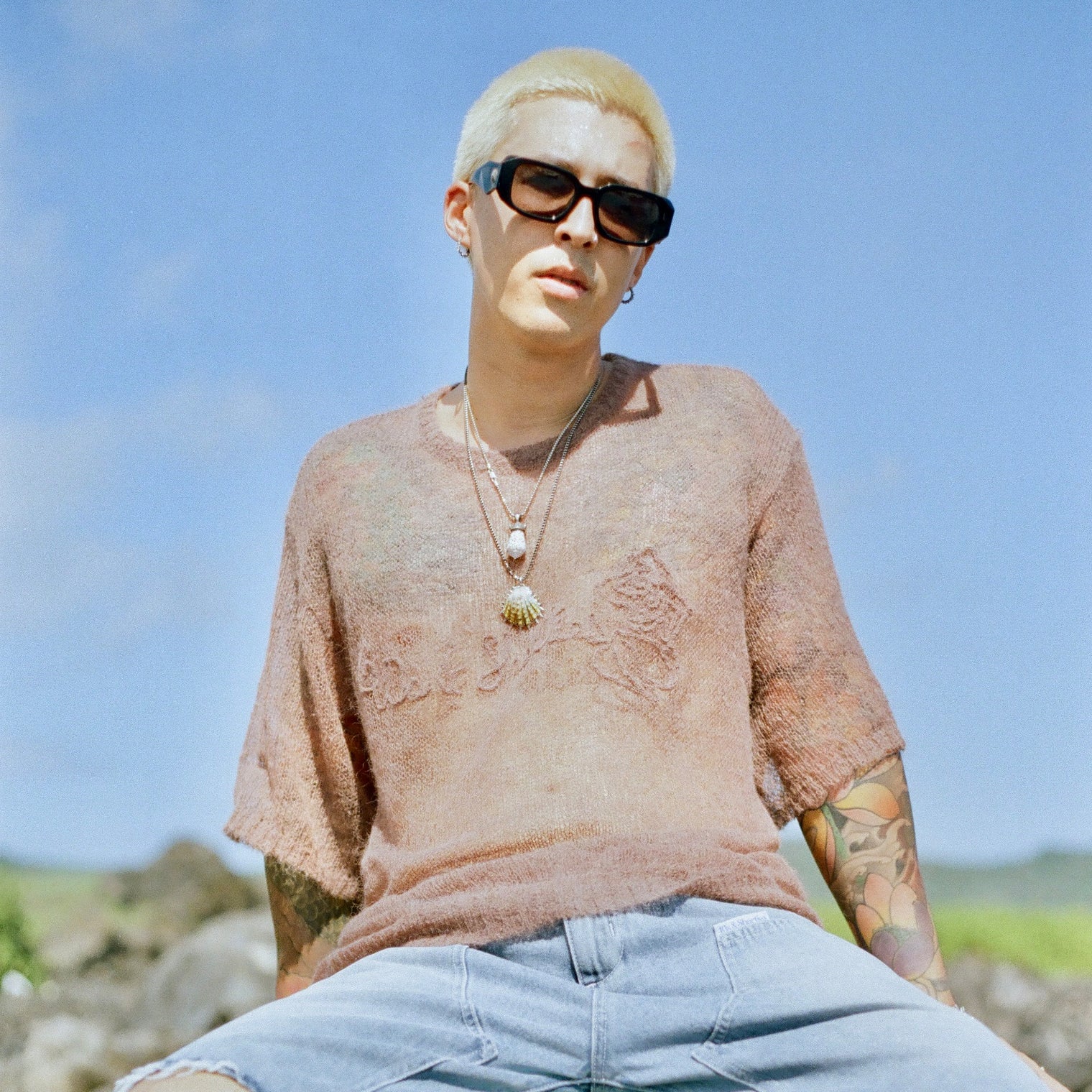Model wearing Fade Away Shirt outdoors with layered necklaces and blue sky background.