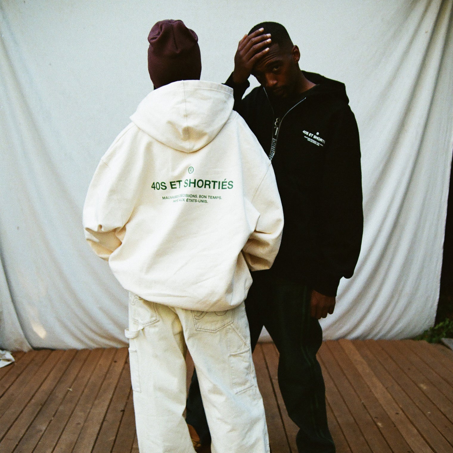 Models facing away wearing French General Zip Hoodies in cream and black, showing bold back text prints – 40s & Shorties.