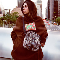 Woman wearing brown Gummy Hoodie and camo crossbody bag on a city street bridge