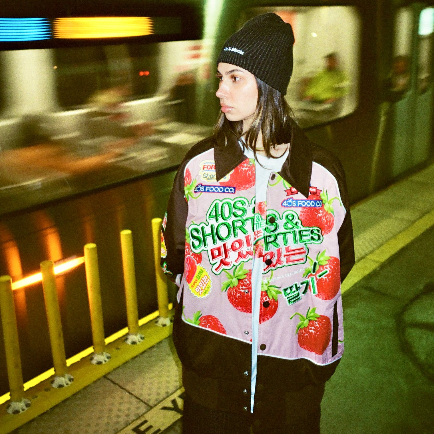 Model wearing Gummy Race Jacket in pink on a subway platform, styled with a beanie