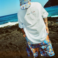 Model wearing Holy Spirit Shorts and matching print cap by the ocean, back view