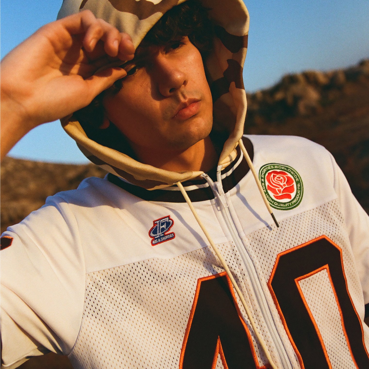 Model wearing 40s & Shorties Jackson Jersey Sweater in Desert Camo with football-style applique numbers and embroidered patches.