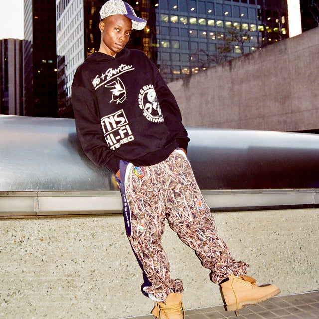 Model wearing the Layout Hoodie on the street styled with patterned pants and boots, city skyline in the background.