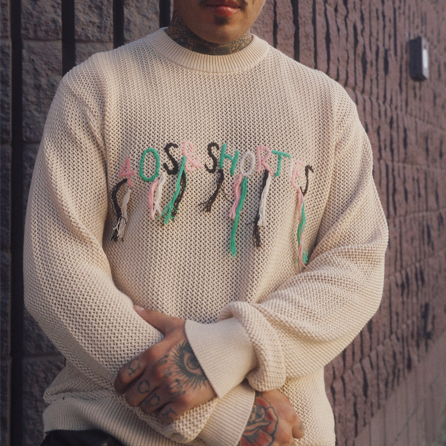 Model wearing the Scribble Logo Sweater in Cream with multicolored loose-thread logo across the chest