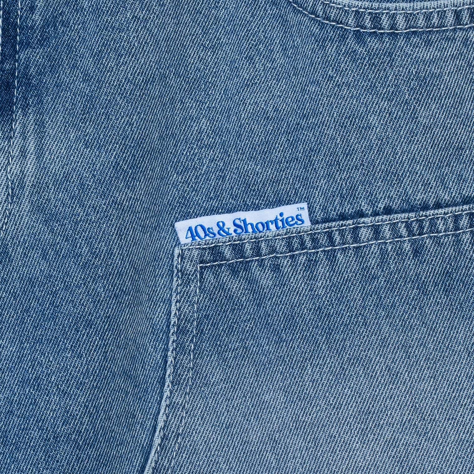 Close-up of 40s & Shorties woven label on front pocket of denim shorts.
