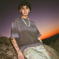 Model in 40s & Shorties Angel Wings Tee black with rhinestone graphics photographed against sunset sky.