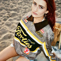 Model wearing Camo Garage Jacket with embroidered racing patches and corduroy collar, seated 
on sand