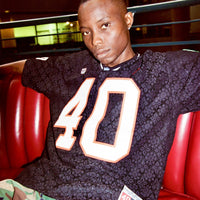 Lifestyle photo: front view of model wearing the Crochet Football Jersey seated in booth