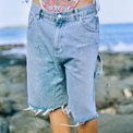 Lifestyle shot of model wearing the denim shorts on the beach, showing front details.
