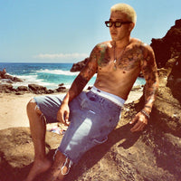 Lifestyle photo of model lounging on rocks in Denim Carpenter Shorts under sunlight.