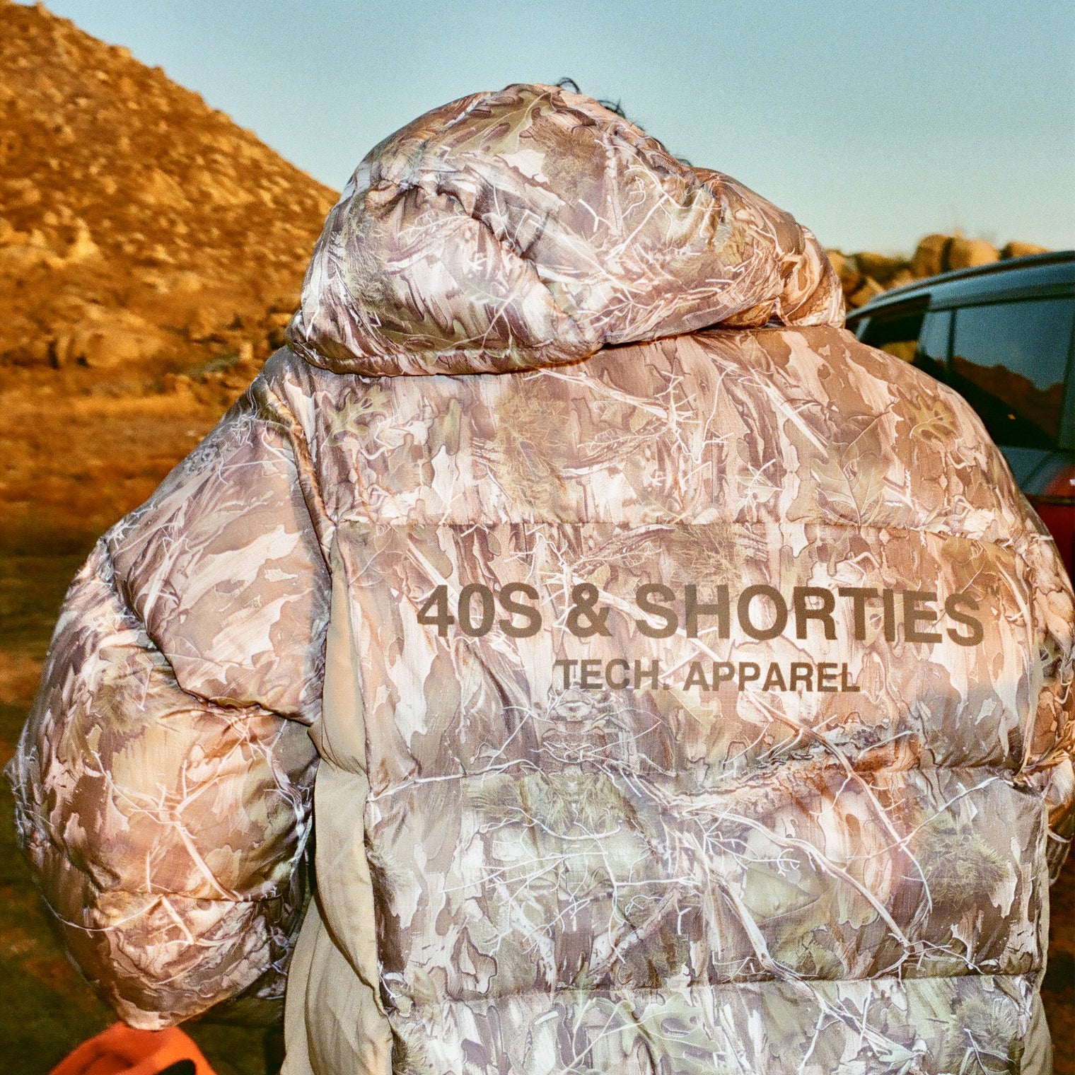 Back view of 40s & Shorties Faded Camo Puffer Jacket showing large printed logo “40s & Shorties Tech Apparel” across shoulders.
