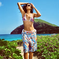 Model in Holy Spirit Shorts and matching bikini top, arms raised, standing by the ocean
