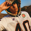 Model wearing 40s & Shorties Jackson Jersey Sweater in Desert Camo with football-style applique numbers and embroidered patches.
