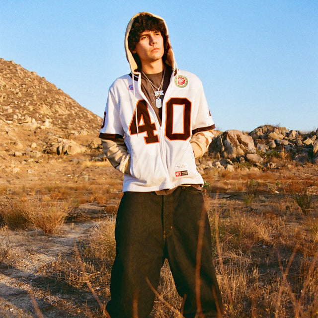 Model standing outdoors in 40s & Shorties Jackson Jersey Sweater Desert Camo with hood up.