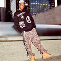Model wearing the Layout Hoodie on the street styled with patterned pants and boots, city skyline in the background.
