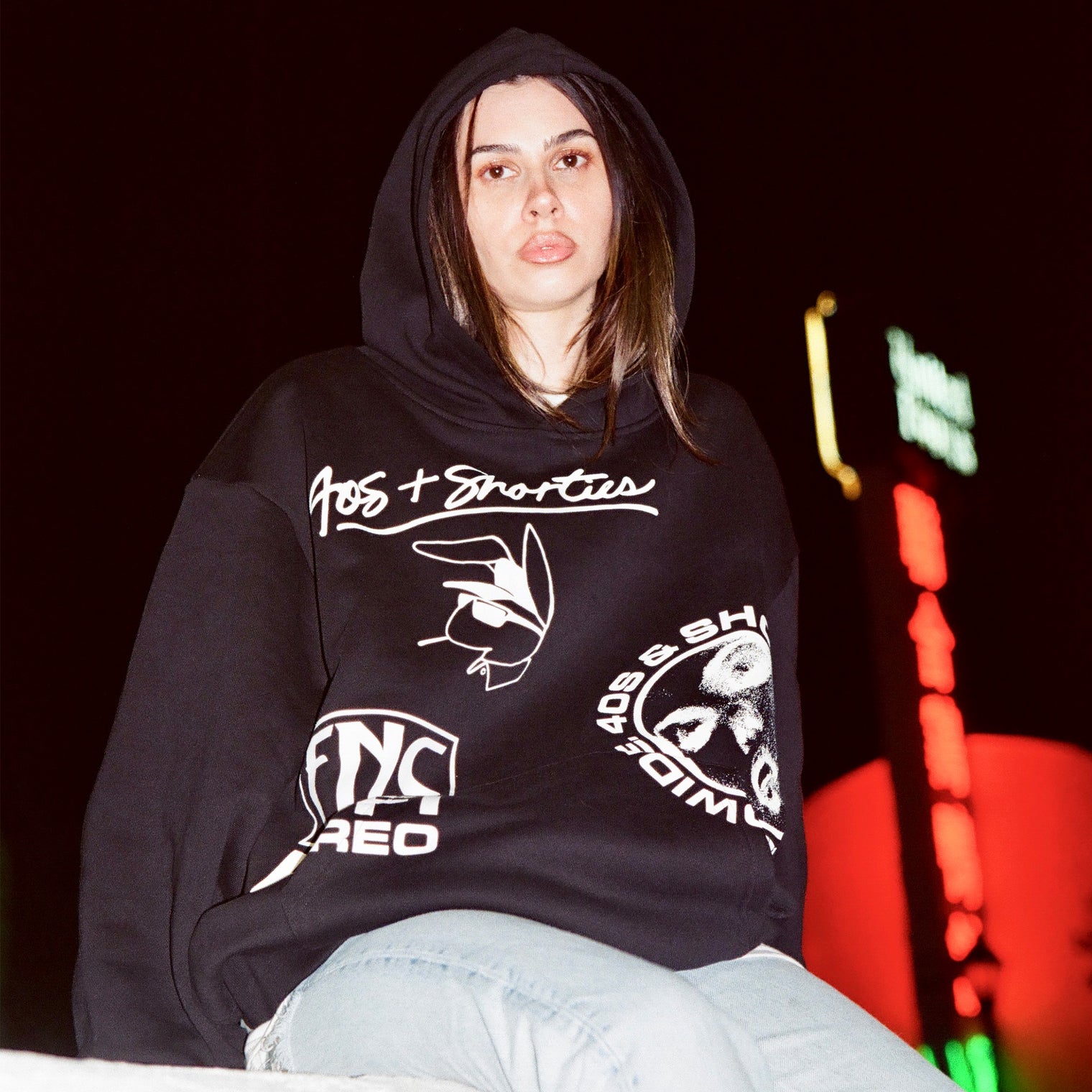 Night shot of a model in the Layout Hoodie with front graphics clearly visible against a city light backdrop.