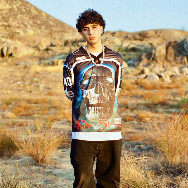 Model in 40s & Shorties Tales Hockey Jersey black with oversized skull artwork and bold sleeve patches, standing in desert landscape.
