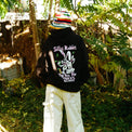 Back view of model in black hoodie with "Silly Rabbit, Tips Are For Tricks" graphic print and colorful knit hat.
